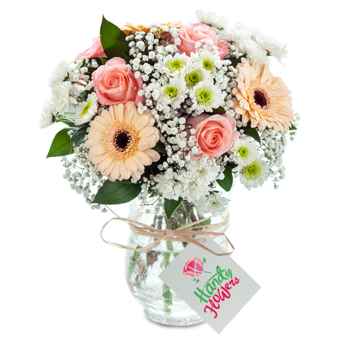 Emanating the sophisticated yet relaxed atmosphere of Primrose Hill, this luxurious floral arrangement features a harmonious tapestry of soft pastels tastefully presented against a crisp white backdrop. At its heart, several robust peach-pink roses bloom in velvet spirals, their blush tones anchoring the bouquet with timeless romance and poise. Flanking them, a pair of radiant peach gerbera daisies offer wide smiles, their dark centres adding striking depth reminiscent of the vibrant blooms found at Primrose Hill Market. Throughout the arrangement, ample sprays of snowy chrysanthemums and ethereal clusters of baby's breath interlace, generating a cloud-like volume and echoing the airy, open spaces of nearby Waterlow Park. Sprigs of lush eucalyptus dot the composition, their rich green hue providing contrast and a natural hint of refreshing aroma. The stems, neatly arranged and visible through a slightly textured glass vase, have an effortless, artisan feel, reflecting both tradition and modern style beloved in the local community. The vase's neck is wrapped with rustic twine, its bow holding a blank white gift tag, allowing for bespoke messages of celebration or sympathy. Beautifully lit and photographed, this bouquet speaks of thoughtful curation, freshness, and a genuine neighbourhood touch-ideal for home decor, anniversary gifts, or heartfelt deliveries to friends and loved ones around Primrose Hill.
