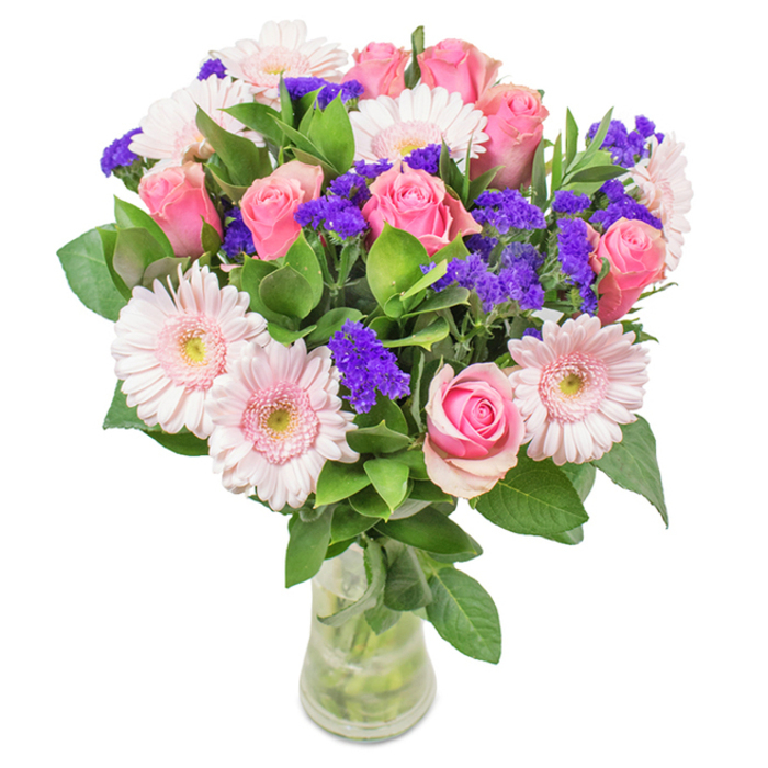A striking, expertly composed arrangement from the florists of Primrose Hill, this bouquet stands in a clear glass vase set against a clean background-its simplicity highlighting the artistry within. Look closely: about seven to nine pink roses are gathered, many tightly furled or just beginning to unfold, their spiral centers drawing admiration like the gentle curves of Chalcot Crescent. Interwoven are five to seven pale pink Gerbera daisies, their large, ruffled heads and lighter centers creating a luminous focal point reminiscent of cherry blossom days in Primrose Hill Park. Vibrant purple statice clusters spring up between the larger blooms, introducing lively pops of color and unique texture that suggest the bouquet has been gathered at one of the area's Sunday flower markets. Deep green, leafy foliage surrounds the blooms, adding rich density and a fresh woodland scent. The pristine vase-its clarity revealing healthy stems and cool, clean water-emphasizes the bouquet's contemporary elegance, perfect for those seeking a stylish floral gift or uplifting home accent for any special occasion in Primrose Hill. Whether presented for an anniversary, Mother's Day, or simply to impart joy, this bouquet radiates warmth, celebration, and a sense of cherished local tradition.